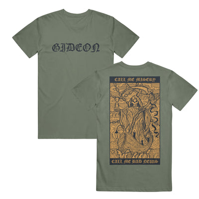 a green moss colored t shirt. The text "GIDEON" is printed in black heavily stylized text on the front. There is a large yellow rectangle on the back. The header of the rectangle has the text "CALL ME MISERY" and "CALL ME BAD NEWS" on the footer. There is a grim reaper holding an hourglass and scythe. He is riding on a small boat. 