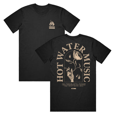 Black t shirt. The top right has a small campfire graphic. The back of the shirt has the band name "HOT WATER MUSIC" arched around a hand holding a rose. There is also very small text underneath the main design that is unreadable in the photo.