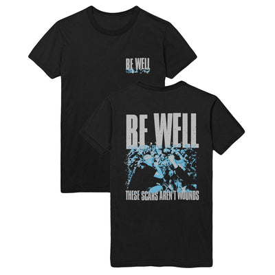 A black t shirt. The front of the shirt has a small design on the top right. The words "BE WELL" are printed in grey. Underneath the text is a blue splattered design. The back of the shirt has a large design. the text "BE WELL" and "THESE SCARS ARENT WOUNDS" printed on the top and bottom. The middle of the shirt has a design of the vocalist singing knelt down to the crowd in black and blue colors.