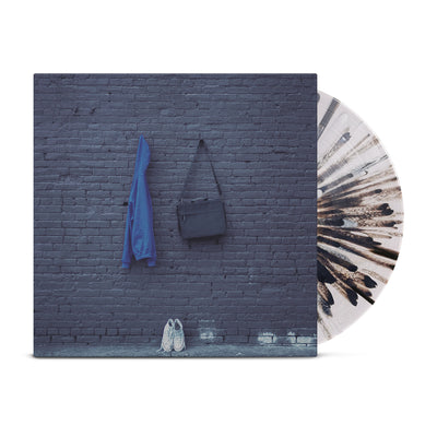 Clear vinyl with black splatter around it. Jacket of vinyl is a picture of a gray brick wall. A blue hoodie and black bag are hanging from the center of the brick wall. A pair of white sneakers are placed on the ground against the wall.