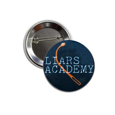 A small circular black pin. on the pin is the text "Liars academy". Behind the text is a red object with a circular point. The point is tied by a wire to an end that looks like the hole you would find in a needle.