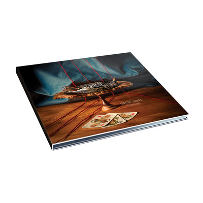 CD depicting a dead bird on a serving tray. Next to the tray is 3 playing cards. All of this is on top of a table.
