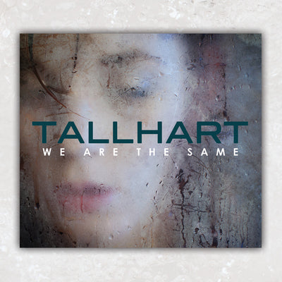 A cd case. The album art is a photo of a person looking through frosted over glass. The text "TALLHART" is printed in green> The text "WE ARE NOT THE SAME" is printed in white underneath the band name.